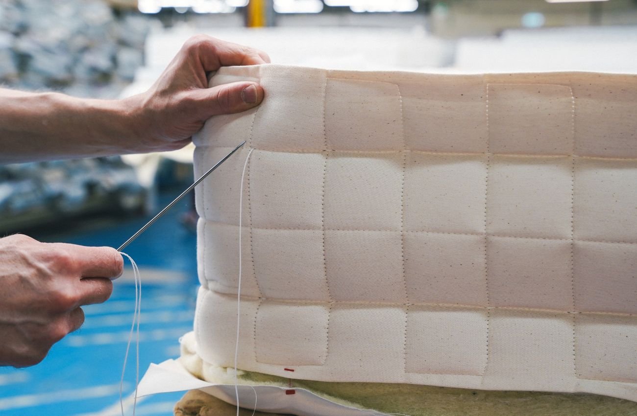White man's hand stitching together a mattress with a large sewing needle