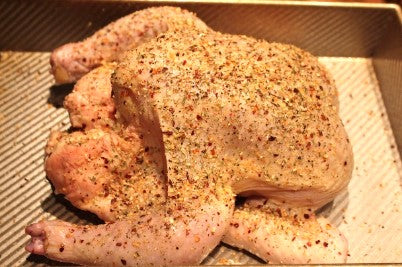 Whole seasoned chicken in a roasting pan.