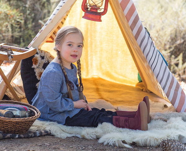 Little girl with Down Syndrome wearing boots by a tent