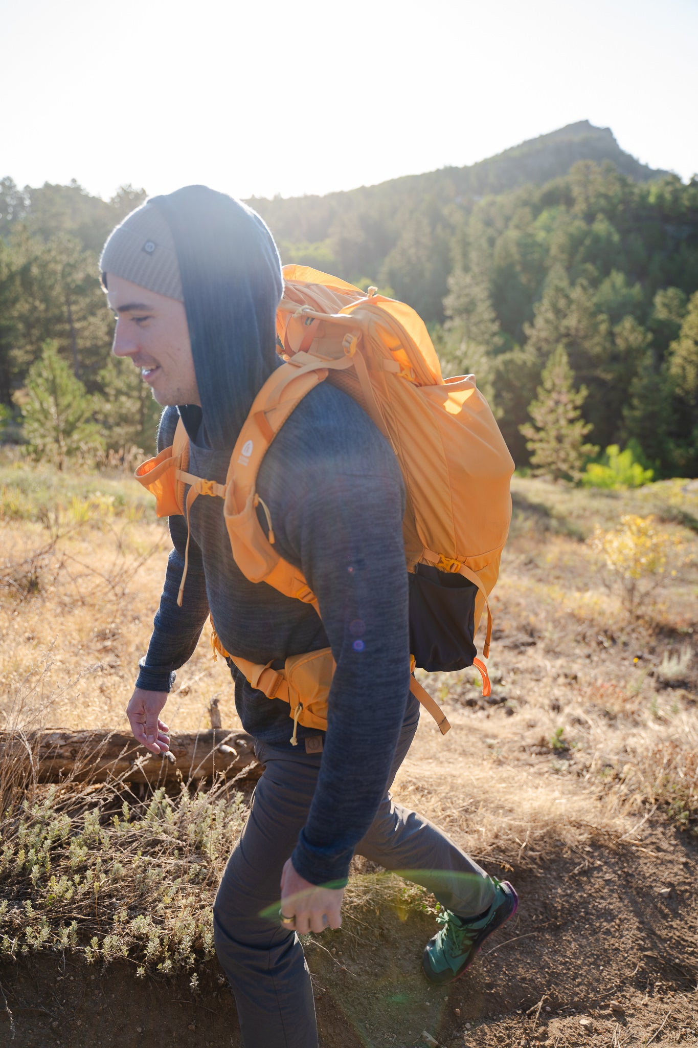 Person hiking with an orange backpack on a sunny day in a forested area.