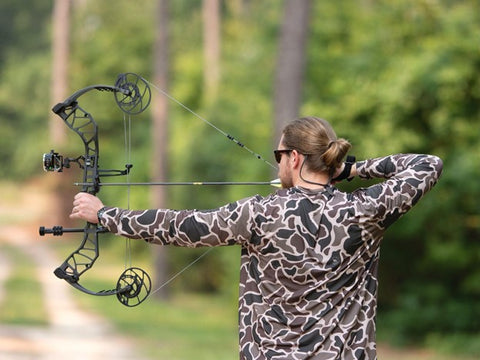 Man in camouflaged hunting shirt with crossbow aimed