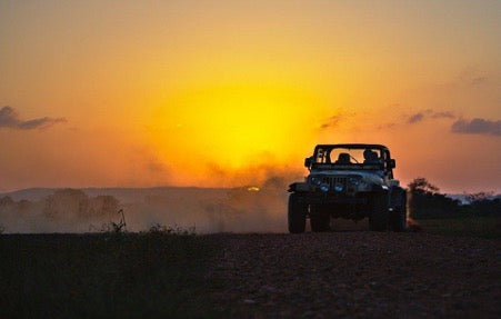 An off-road vehicle on a dusty track at sunset