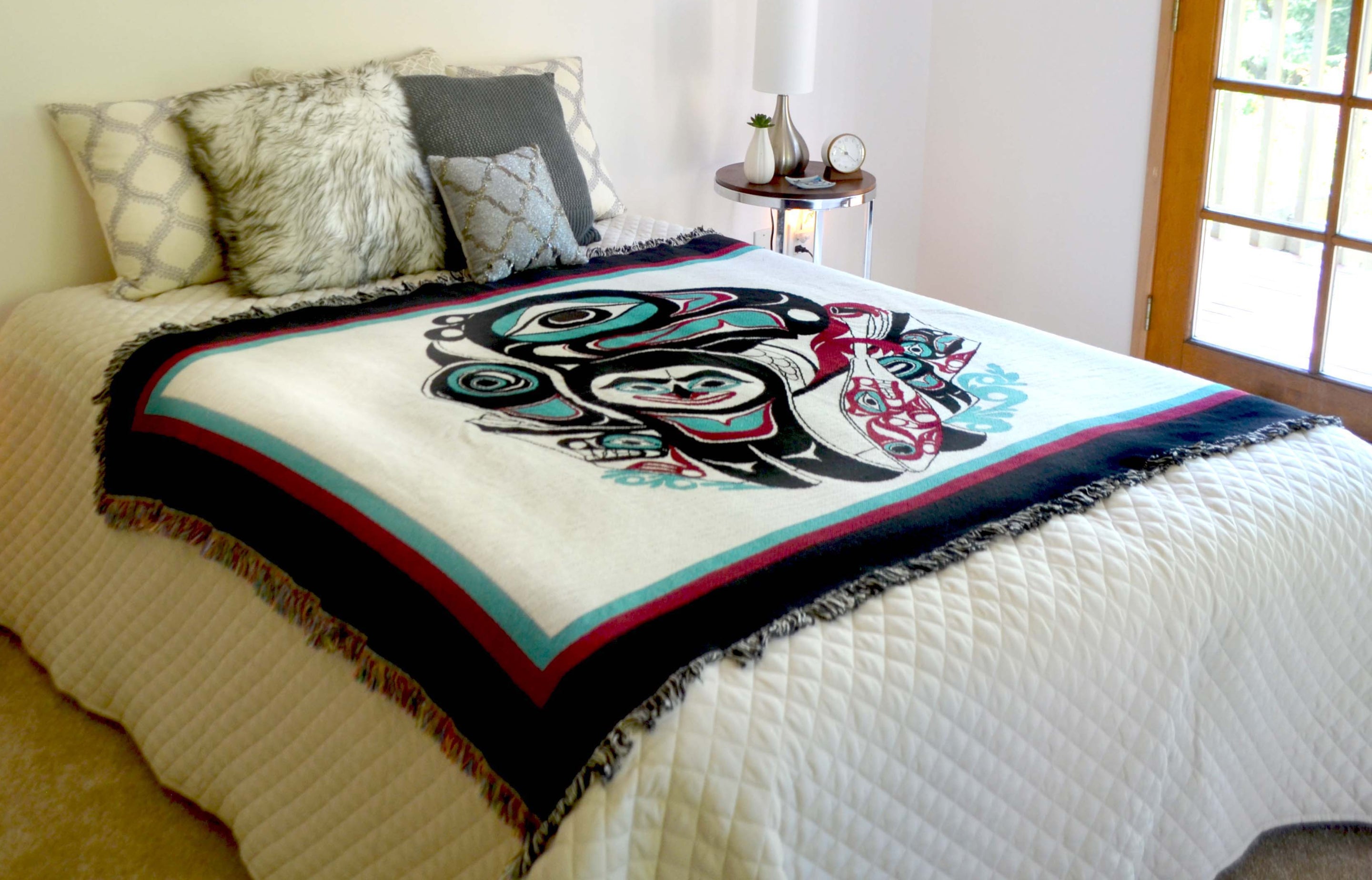 Going to the Potlatch Art Tapestry Throw Blanket on a bed with Shotridge Art Prints on walls