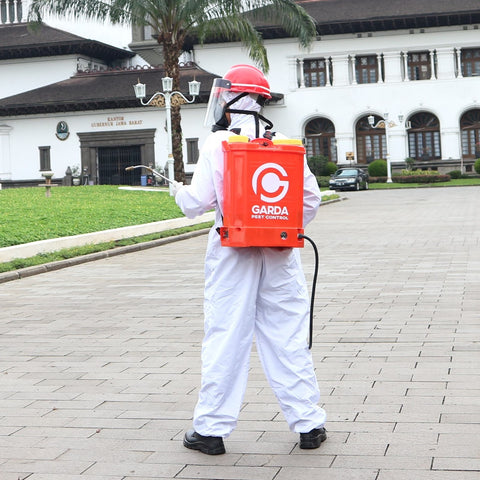 A person spraying pesticides while wearing coveralls, gloves, respirator mask, helmet, and face guard.