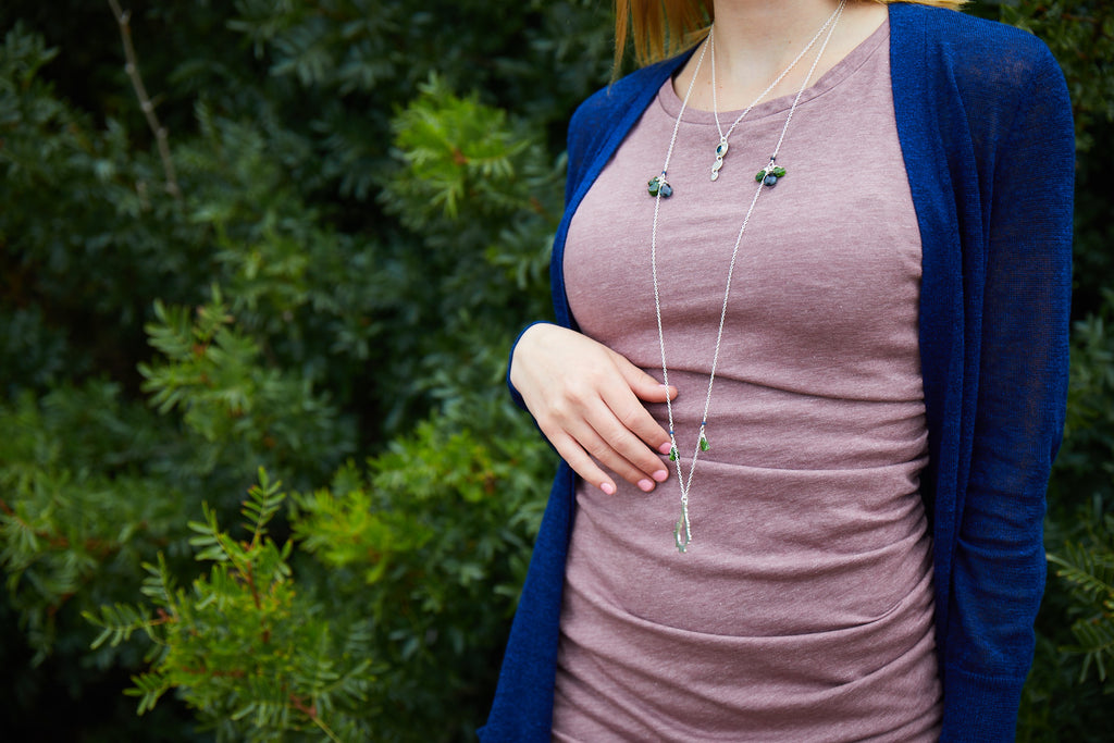 jewelry model wearing long sterling silver pendant necklace and short silver round pendant necklace in front of trees 