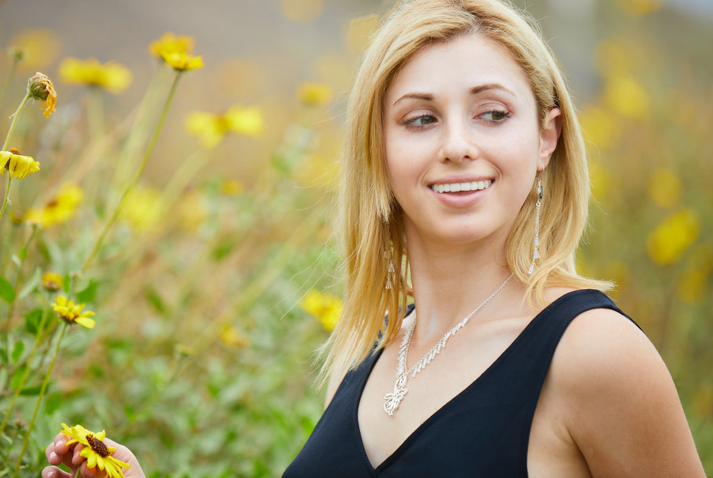 jewelry model wearing short sterling silver pendant necklace and sterling silver chandelier earrings in a field of daisies