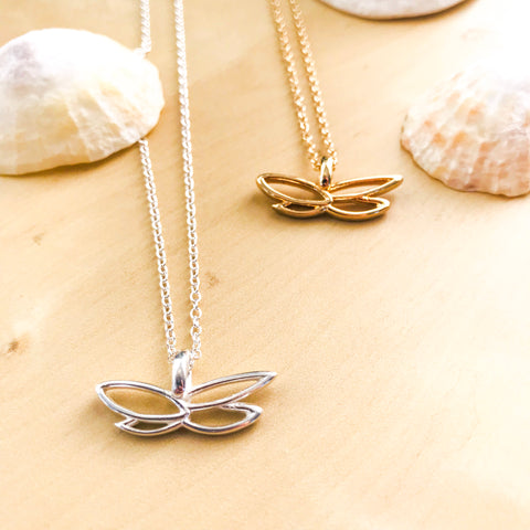 Butterfly for Breast Cancer Research Necklace in Silver and Gold on a table with shells