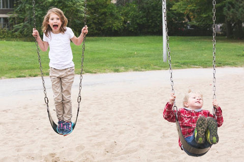 brother and sister on swings in a park