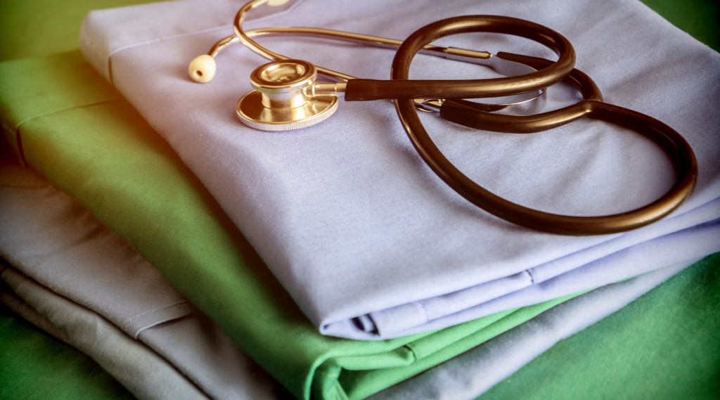 Pile of white and green customiz apparel (scrubs) for healthcare worker with a coiled stethoscope on top.