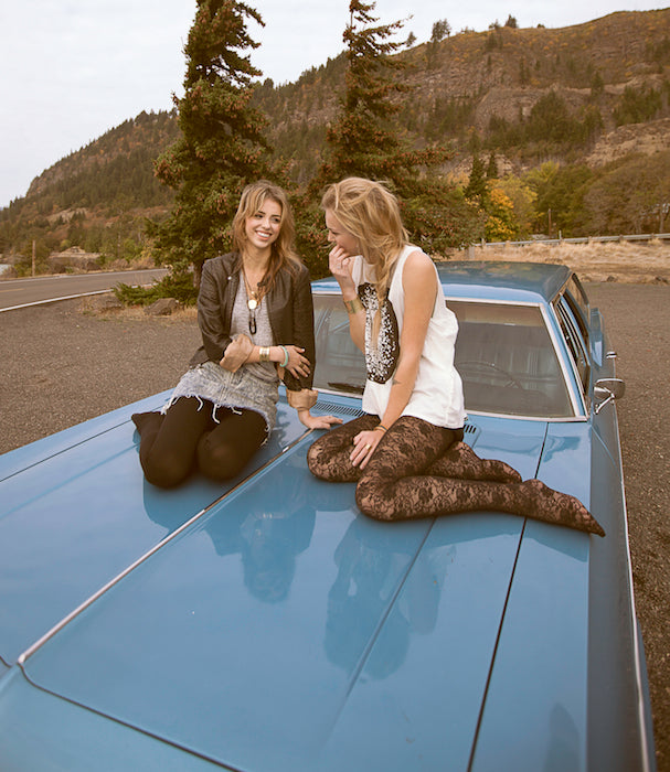 Models hanging out on the top of a vintage car.