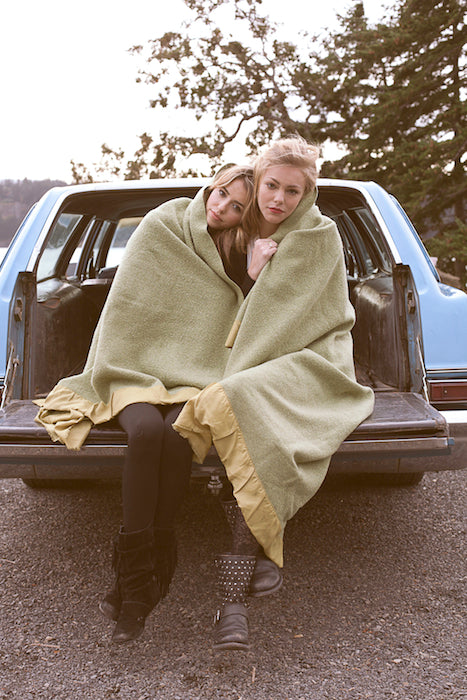 Models sweetly cuddling with a blanket on the back of a vintage car.