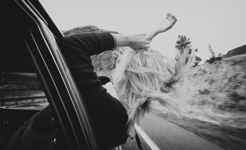 Model's hair blowing in the wind as she sticks her head out of a moving car.