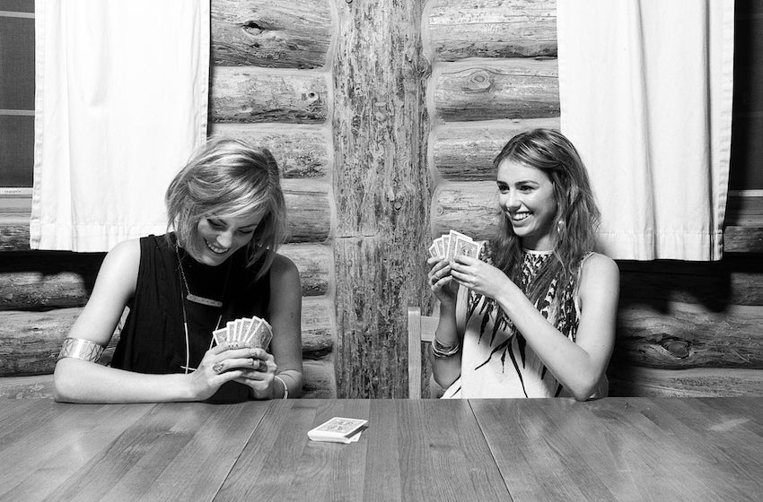 Models giggling while playing cards in a cabin.