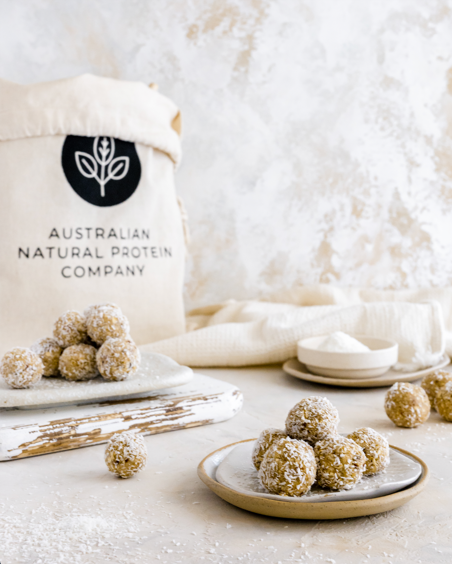 Pictured are freshly made vanilla bean protein bliss balls on a plate with Australian Natural Protein Company Package of Organic Vanilla Bean Protein Whey Powder in the background