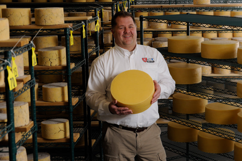 Man standing with wheel of aged cheese in cheese cellar