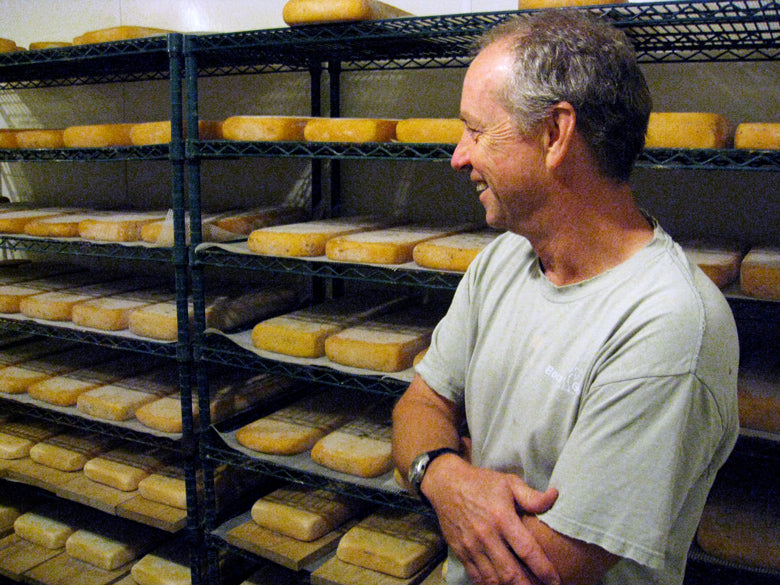 Man smiling looking at racks of cheese in a cheese cave