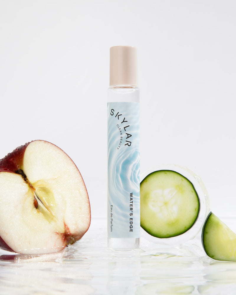 Water's Edge fragrance: Travel-size bottle with a fresh fruity scent next to apples and cucumber.