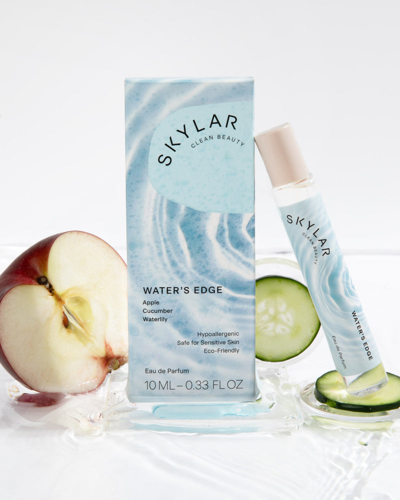 Water's Edge fruity fresh travel-size fragrance with its box next to apple and cucumber.