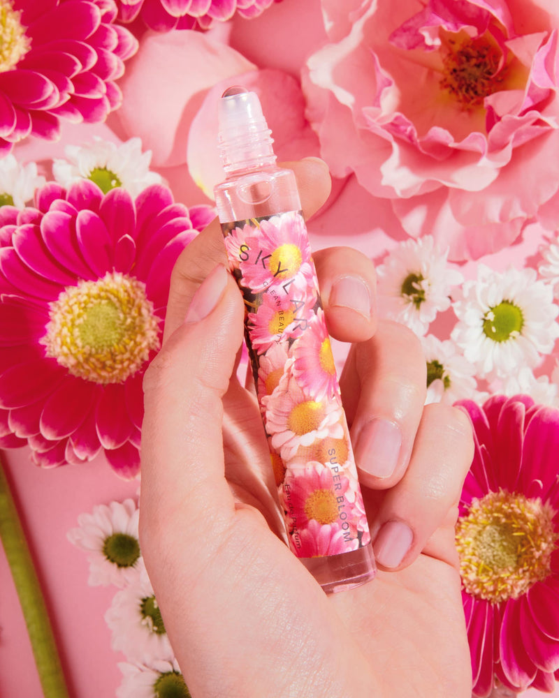 Woman holding Super Bloom floral fragrance in a travel-size bottle surrounded by flowers.