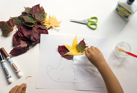 Picture of a kid hand gluing leaves to a hedgehog