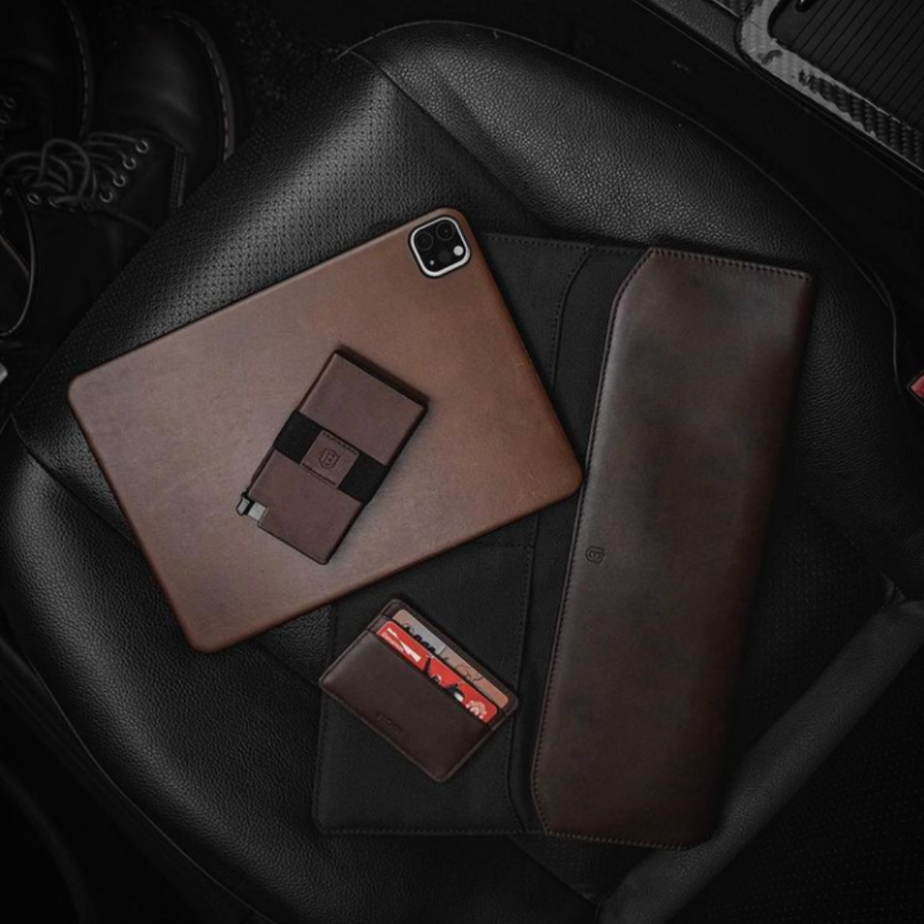 A brown leather wallet, iPhone case, and laptop sleeve on a carseat.