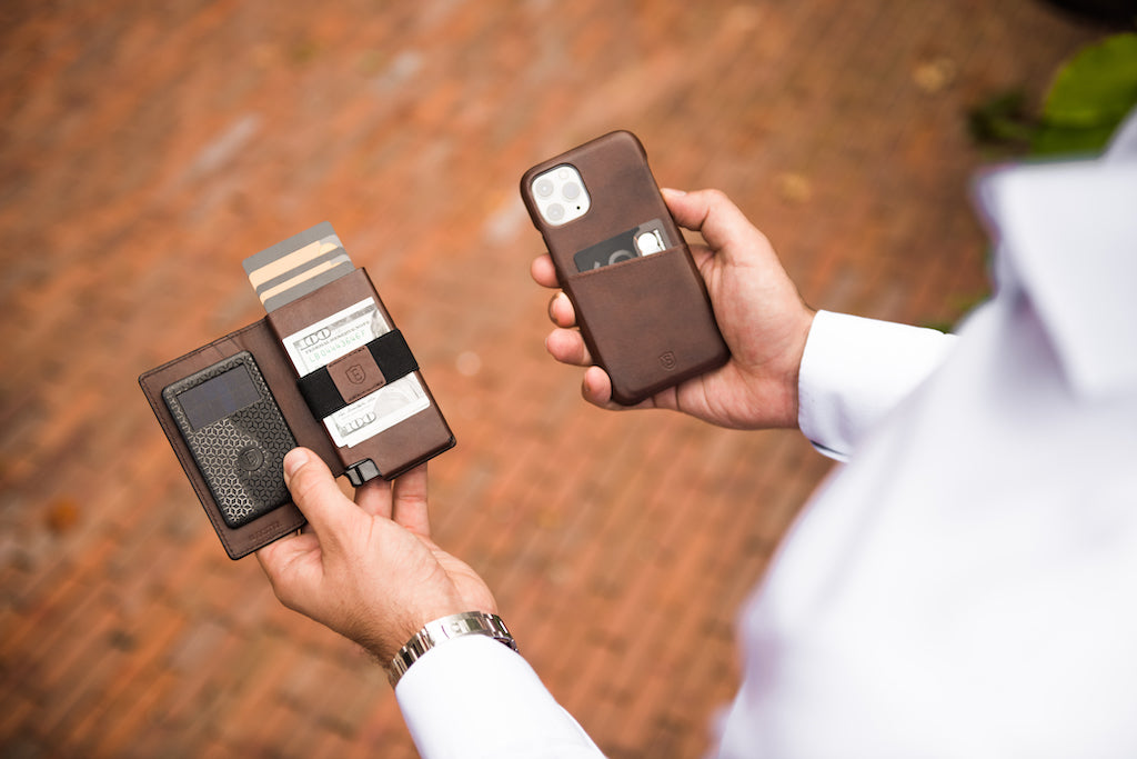 A man's hands holding a slim leather wallet in his left hand and an iPhone with leather case in his right. 