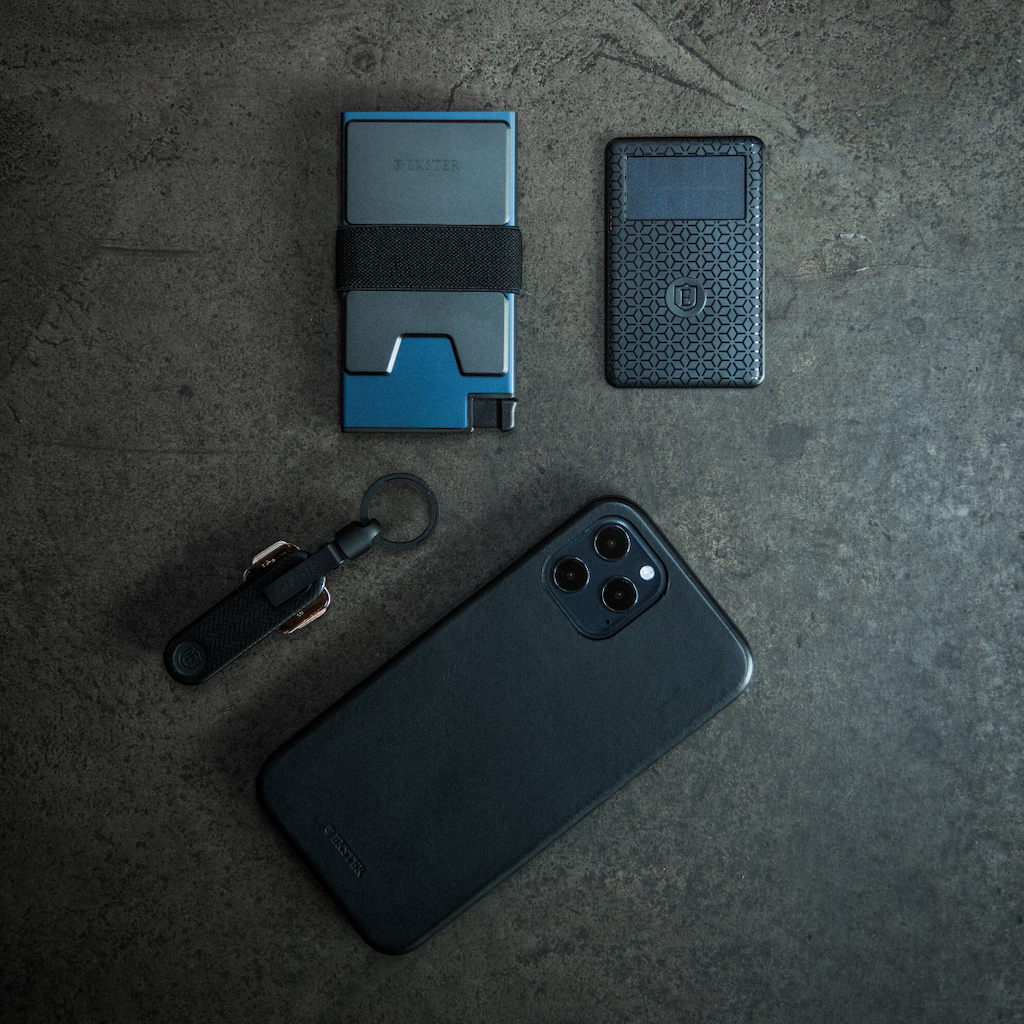 blue aluminum wallet, wallet tracker, key case, and iphone lying on concrete