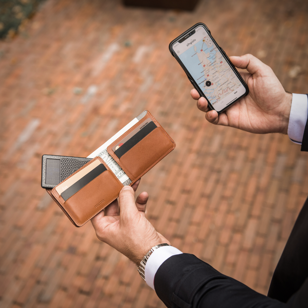 Person's hands holding an iPhone with Chipolo tracking app and Ekster Bifold wallet with tracker card