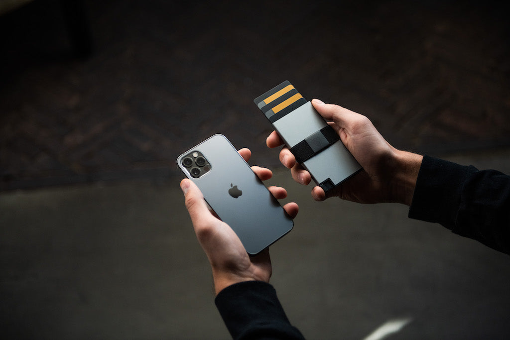 A man's hands holding an iPhone in his left hand and an aluminum cardholder in his right hand.