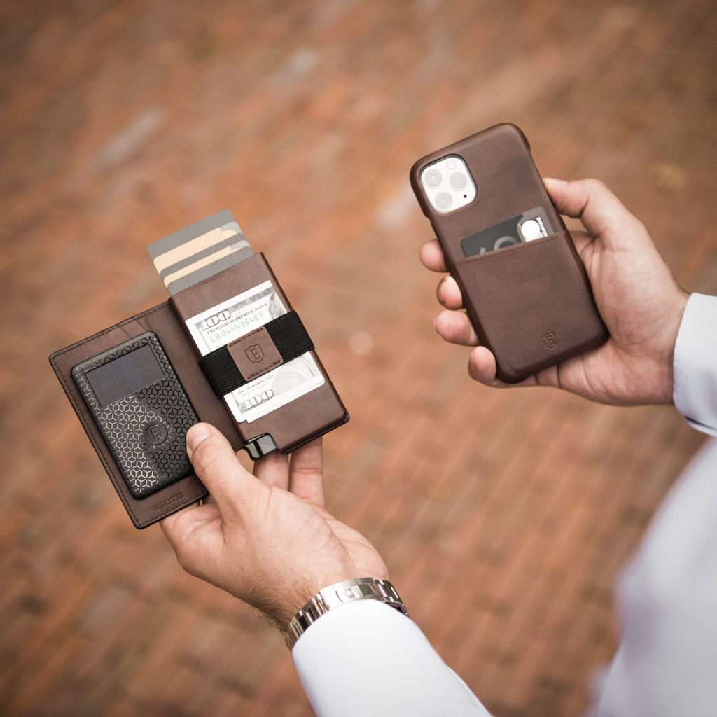 Man's hands holding a slim brown leather wallet in one hand and an iPhone with a brown leather case in the other. 