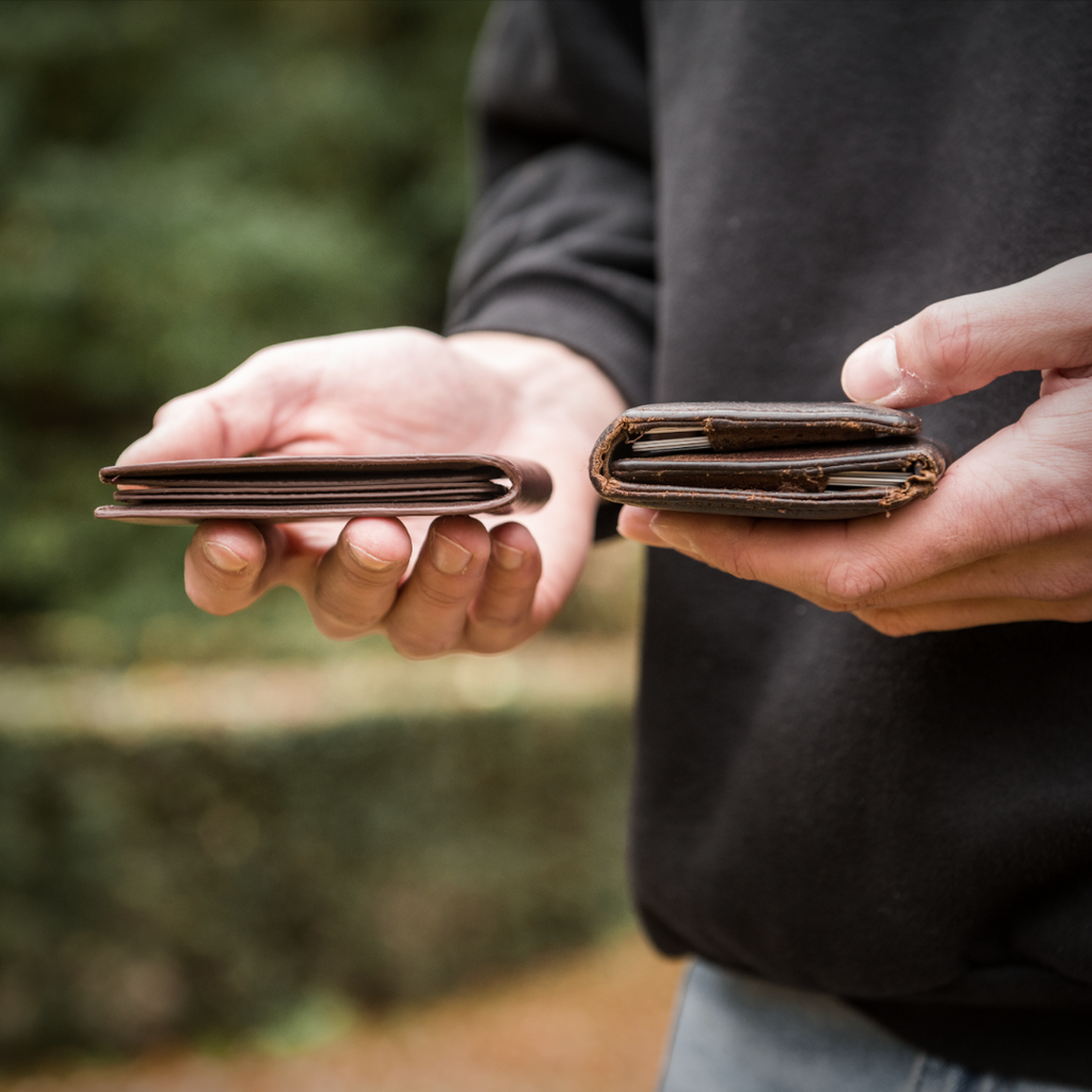 Pictured are a man's hands holding two wallets. In his left hand he is holding a leather bifold wallet that is visibly thicker than the wallet in his right hand. The picture shows how much thinner Ekster's Modular Bifold is than other bifold wallets.