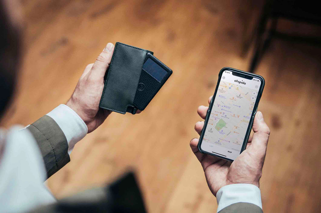 The image shows a man holding an Ekster smart wallet in his right hand. The Ekster wallet is in Juniper Green and has the Ekster tracker card for never losing your wallet peeking out of it. In his left hand he is holding an iPhone which is opened up to the tracking app.