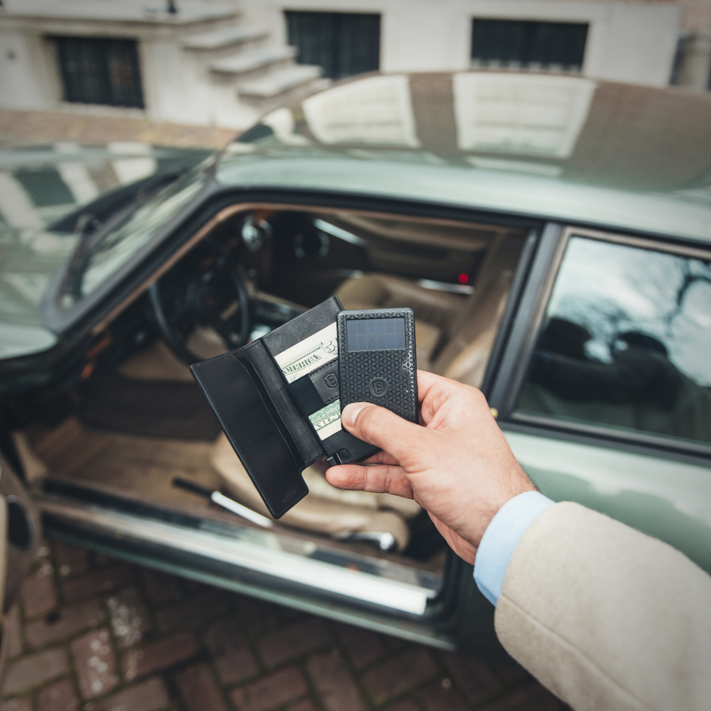 Man holding a slim leather wallet and tracker card for wallet in his right hand. 