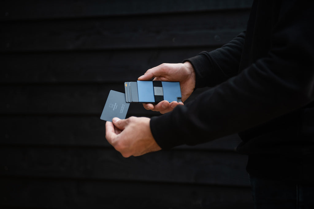 A man using his left hand to remove a card from an aluminum cardholder wallet.