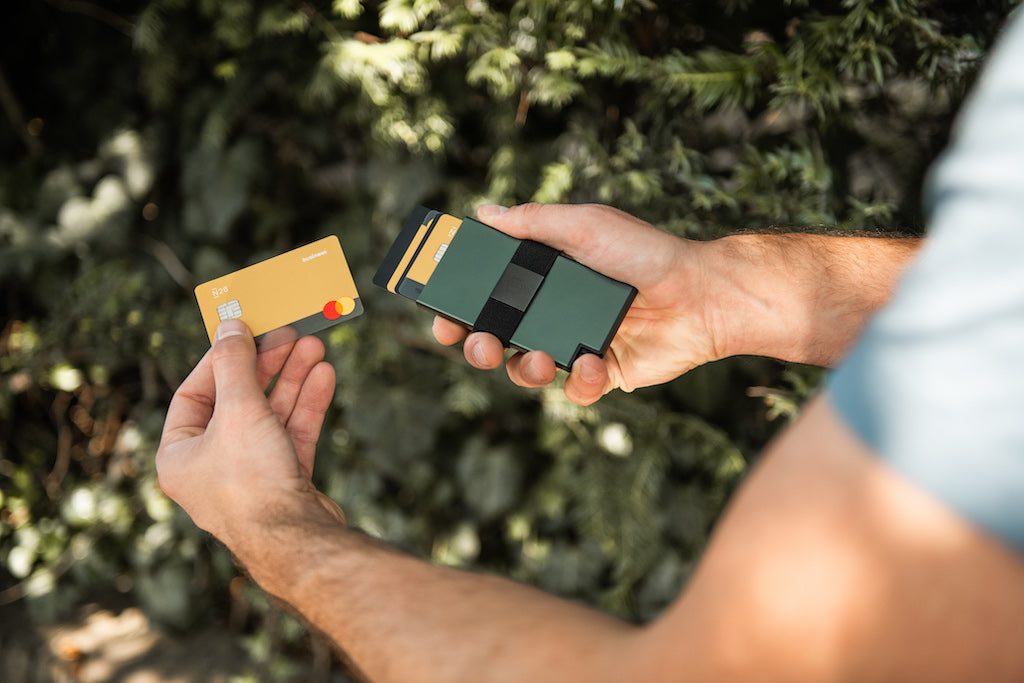 A man holds a green Ekster aluminum cardholder in one hand and removes a card from the wallet with the right hand. 