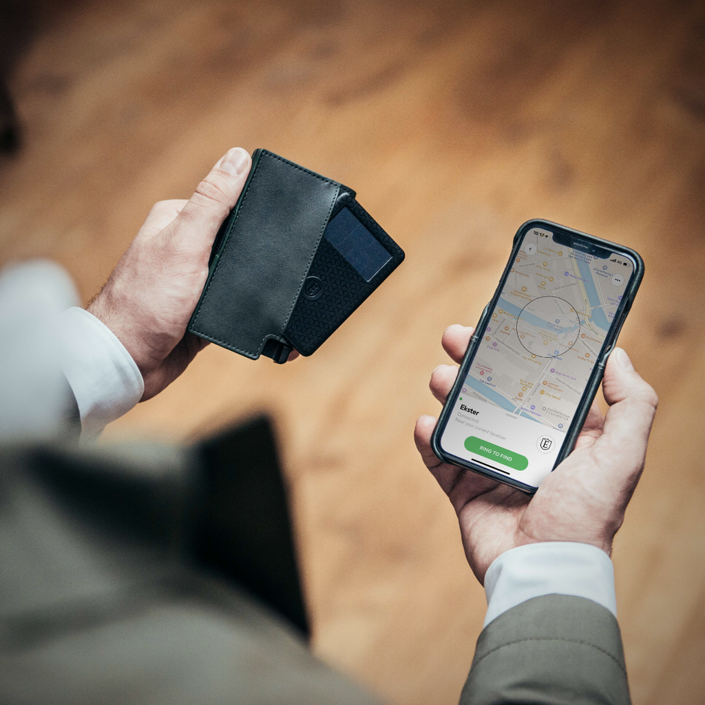A man's hands holding a slim leather wallet with a wallet tracker in his left hand and an iPhone showing a map in his right hand.