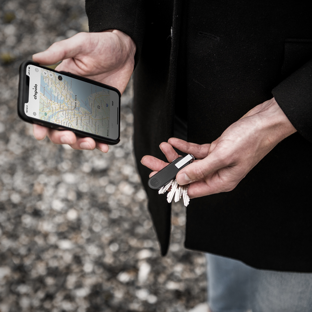 Pictured is a man hands holding in his left hand an Ekster Key Holder and Tracker and in his left, an iPhone displaying a map for tracking your keys.