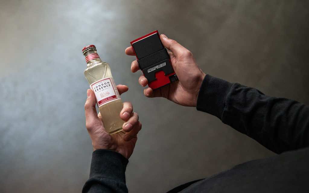 Person’s hands holding liquor and RFID-blocking black red aluminum cardholder x Angry Joe Show collaboration

