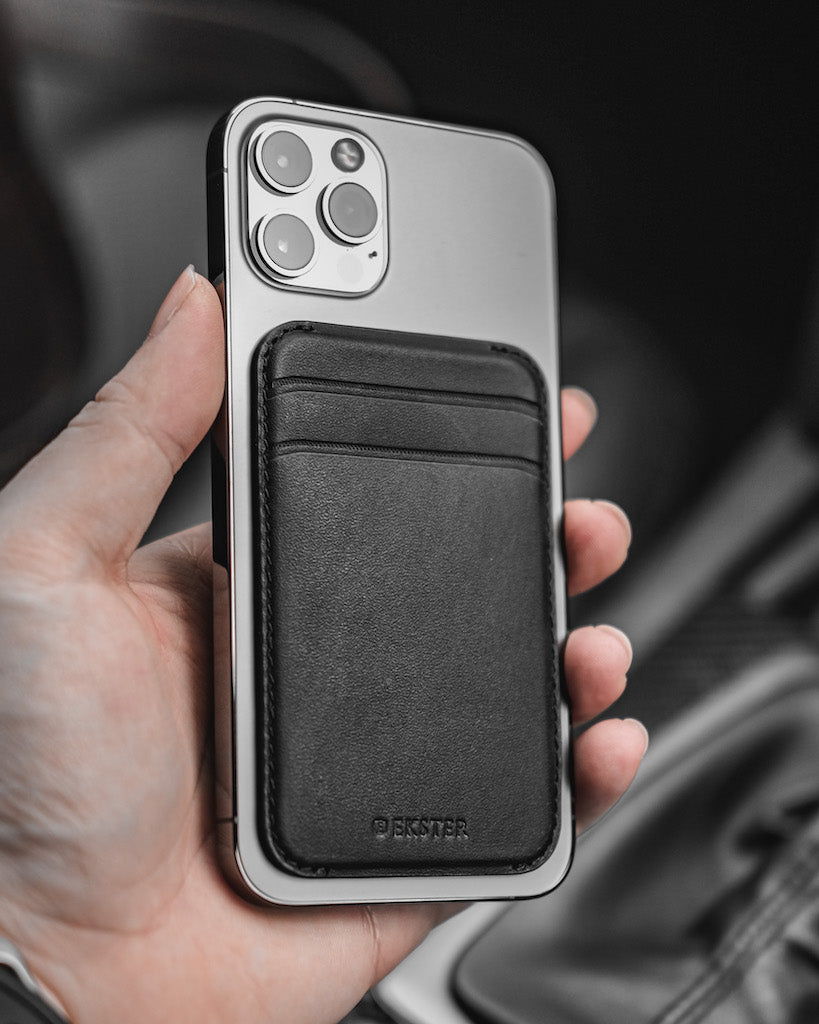 A man's hand holding an iPhone with MagSafe Cardholder attached to the back.