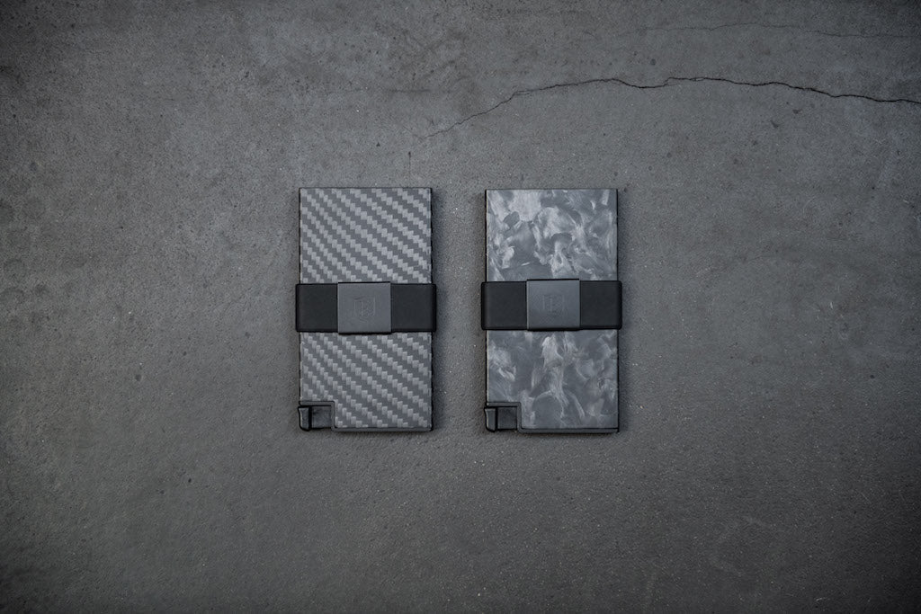 two carbon fiber card holder wallets lying next to eachother on a concrete background.