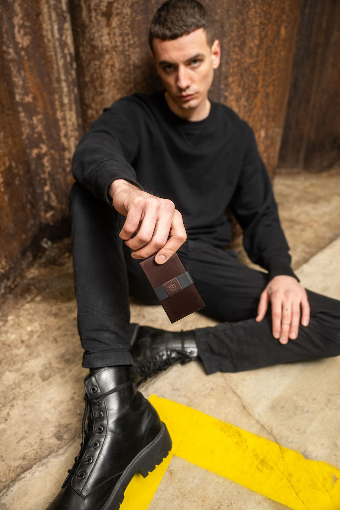 man in black outfit sitting on ground holding copper wallet
