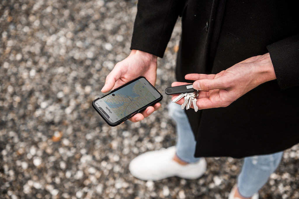 man holding a trackable key fob in one hand and an iPhone in the other