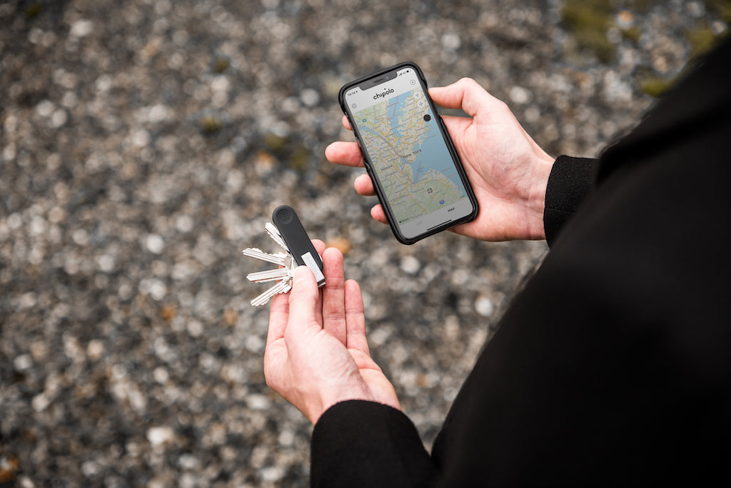 a man holding a bluetooth key tracker in his left hand and an iPhone in his right hand