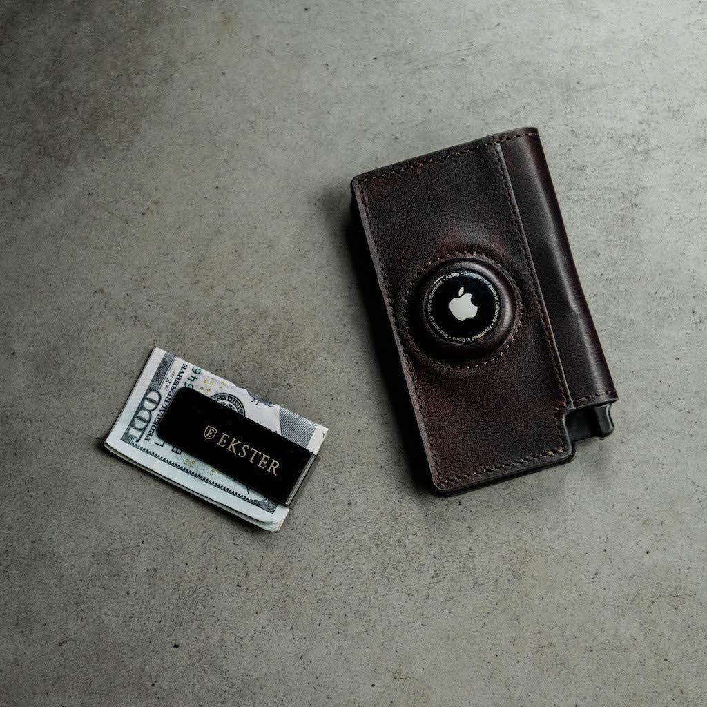 A man's hand holding a slim leather AirTag wallet. 