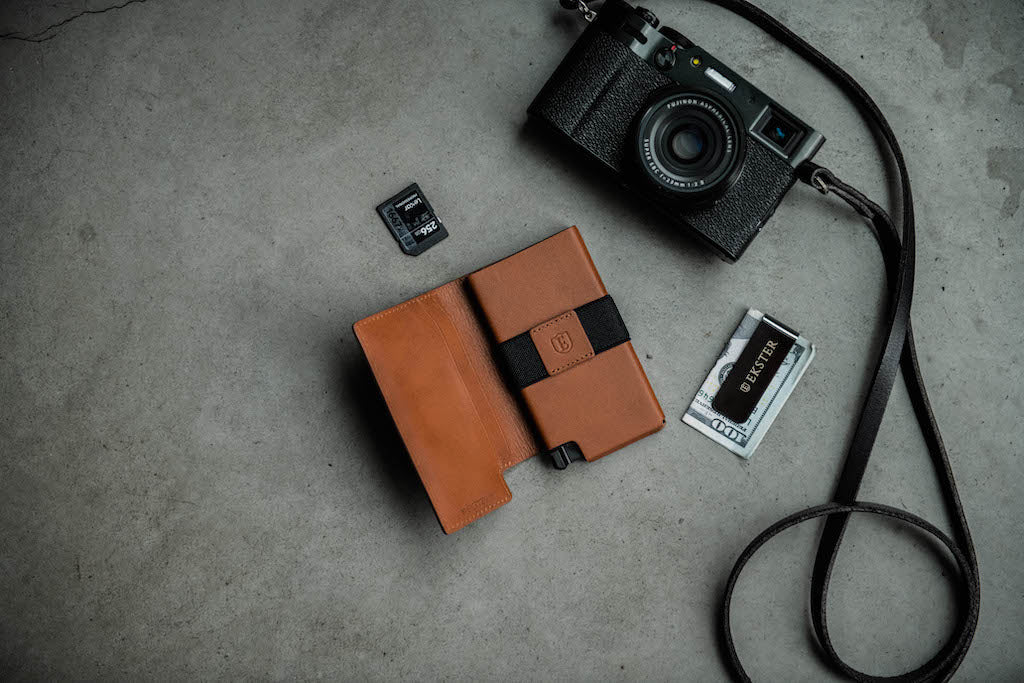 a leather designer card holder wallet lying next a camera, sim card, and cash clip on a concrete surface