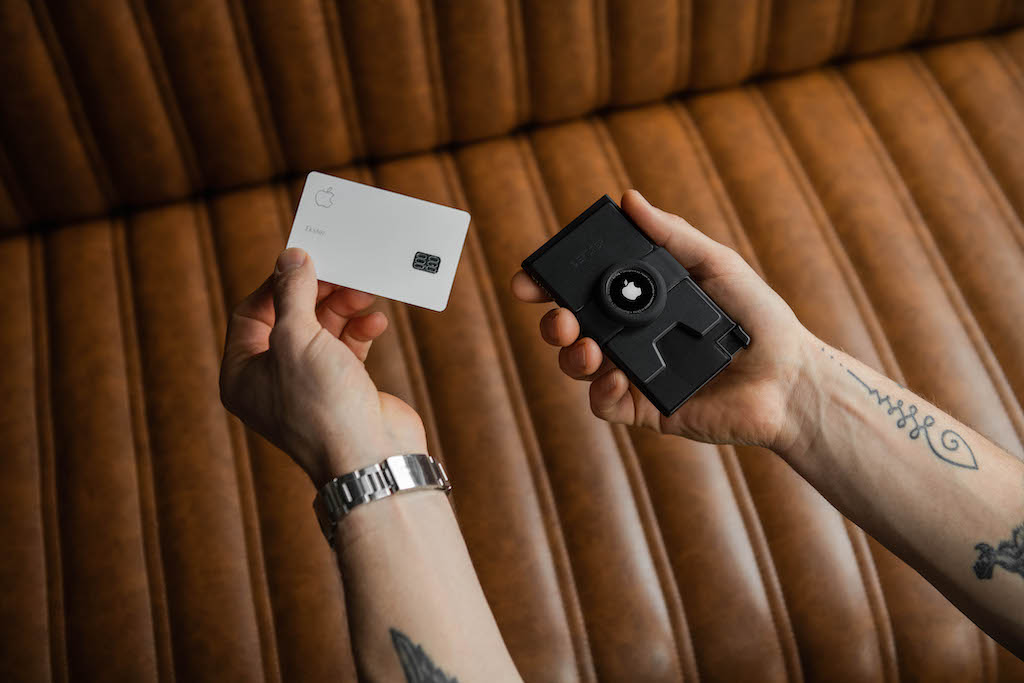 A man's hands, in his right hand he is holding a black airtag cardholder and with his left hand he is removing a card from the airtag cardholder