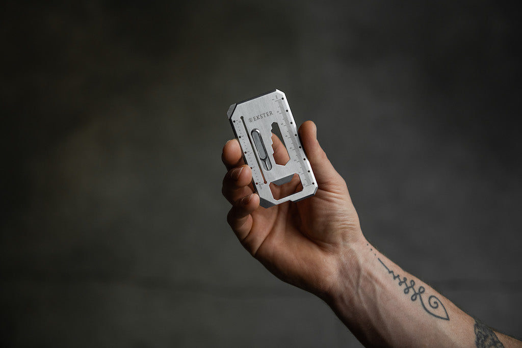 A man's right hand holding a credit card multi tool for wallets.