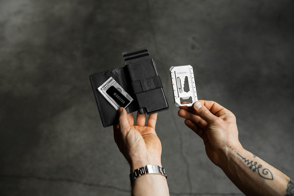 Man holding a slim leather wallet, tool card, and cash clip. 