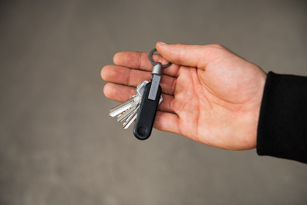 A man's right hand holding a key holder and key tracker from Ekster.