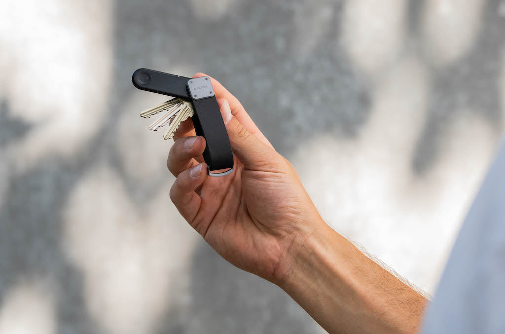 a man's hand holding a bluetooth key finder attached to a key case 